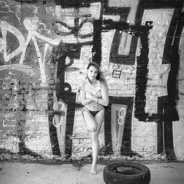 Schwarz-Weiß-Portrait einer Frau in Unterwäsche vor einer Graffiti-Backsteinwand, urban und künstlerisch inszeniert – LensAnd