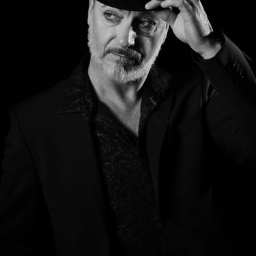 Schwarz-Weiß-Porträt eines Mannes mit Zylinder, Bart und Make-up, der zur Seite schaut.