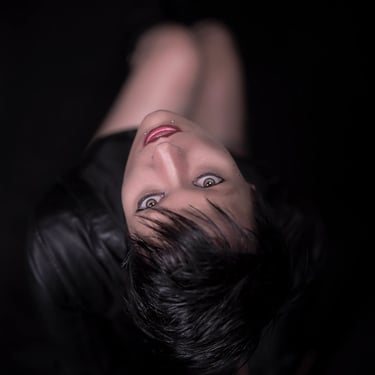 Blick von oben auf eine Frau mit kurzen dunklen Haaren, die nach oben schaut, mit auffälligen Augen und Lippen.