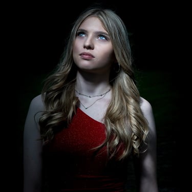 Porträt einer blonden Frau mit blauen Augen, die ein rotes, glitzerndes Kleid trägt und nach oben schaut.