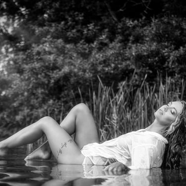 Schwarz-Weiß-Aufnahme einer Frau in einem nassen Hemd, die entspannt im Wasser liegt.