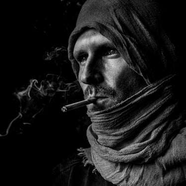 Schwarz-Weiß-Porträt eines Mannes mit Kapuze und Schal, der eine Zigarette raucht.