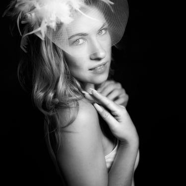 Schwarz-Weiß-Porträt einer Frau mit Federn und Schleier, die über die Schulter blickt.