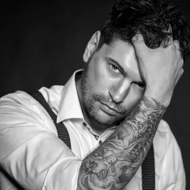 Schwarz-Weiß-Porträt eines Mannes mit tätowiertem Arm, der sich die Hand an die Stirn hält.