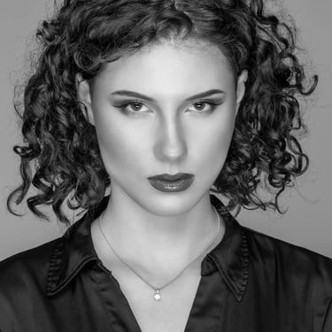 Schwarz-Weiß-Porträt einer Frau mit lockigem Haar, dunklem Hemd und einer Halskette mit Anhänger.