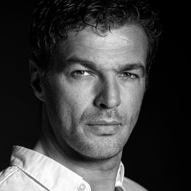 Schwarz-Weiß-Porträt eines Mannes mit dunklen Haaren, der direkt in die Kamera blickt.