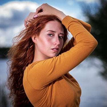 Porträt einer rothaarigen Frau mit Sommersprossen, die die Hände über dem Kopf hält und in die Kamera blickt.