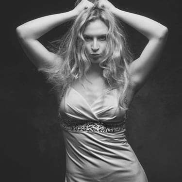 Schwarzweißes Studio-Portrait einer Frau mit erhobenen Armen und intensivem Blick