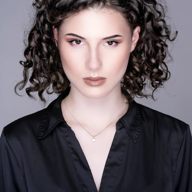 Studio-Porträt einer jungen Frau mit lockigem Haar und elegantem Ausdruck, aufgenommen von LensAndLook – klarer, moderner Loo