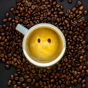 A happy mug of coffee placed amongst freshly roasted coffee beans