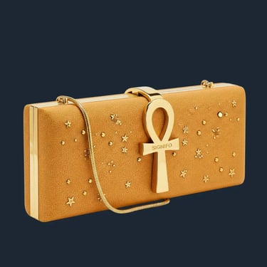 Clutch kotak berwarna kuning busuk dengan hiasan bintang emas dan kuncian ankh di latar putih.