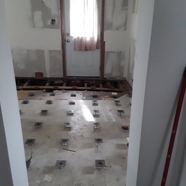 Entryway floor renovation with exposed joists and grid of adjustable pedestal supports for subfloor levelling