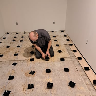 Contractor installing adjustable pedestals for precise subfloor leveling during home renovation