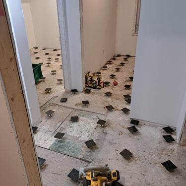 In-progress subfloor leveling installation using adjustable pedestal system during interior renovation