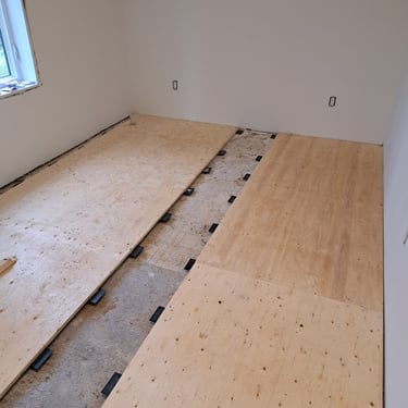 Plywood subfloor installation over leveling mounts during residential room renovation