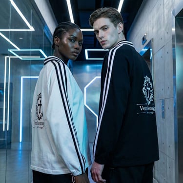 Fashion models wearing branded streetwear jackets with stripes in a futuristic neon-lit hallway.