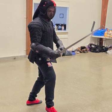 Instructor in full protective gear with steel sword ready for sparring
