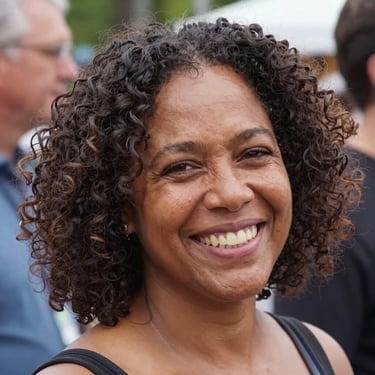 A smiling mature woman with dark curly hair and brown eyes in a close-up portrait.
