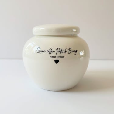 This is a rounded ivory ceramic urn engraved with the text Quinn Alan Patrick Ewing, and adorned with a small heart icon
