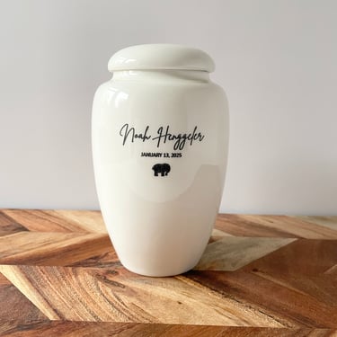 Elegant ivory ceramic urn with soft curves, black script text “Noah Henggeler” and a small elephant icon