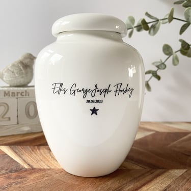 Glossy white ceramic urn with “Ellis George Joseph Fluskey 20.03.2023” and a black star engraved in elegant script.