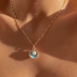 A simple gold necklace with half a shell as a pendant. A pearl hangs from the chain to sit in it.