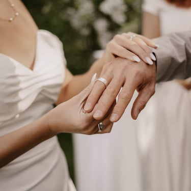 Nahaufnahme der Hände mit Ehering am Finger des Bräutigams, den die Braut gerade ansteckt.