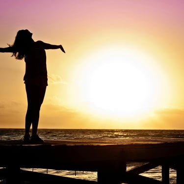 donna al tramonto che guarda il cielo a braccia aperte
