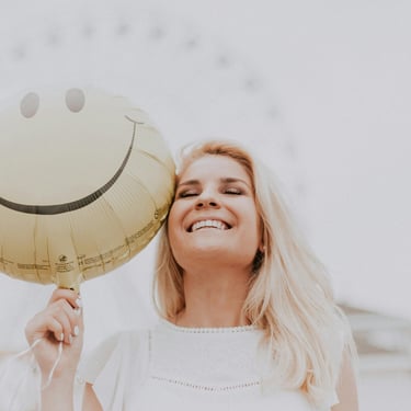 donna bionda sorride con in mano un palloncino a forma di smile