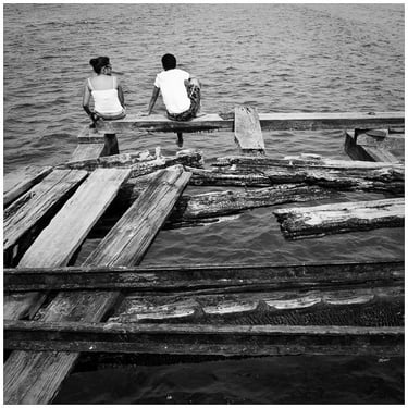 Honduras: two people sitting on a dock with a boat in the water