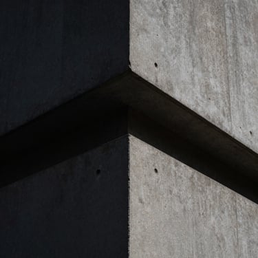 Tight macro shot of sharp concrete architectural angles in London under harsh directional noon light.