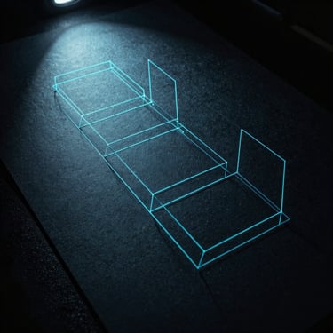 Close-up of physical wireframes on dark textured paper under a sharp neon-cyan spotlight.