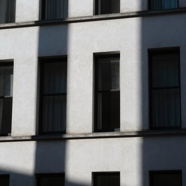 Abstract geometric shadows cast on a stark white London building facade under cool-toned ambient light.