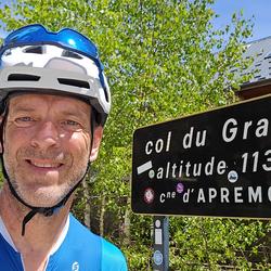 Cyclist posing by a Col du Granier mountain pass sign in the French Alps.