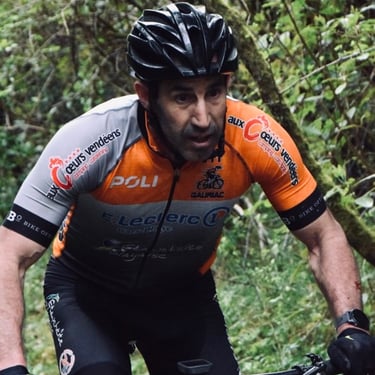 Male cyclist in a black helmet and orange jersey racing a mountain bike on a wooded trail.