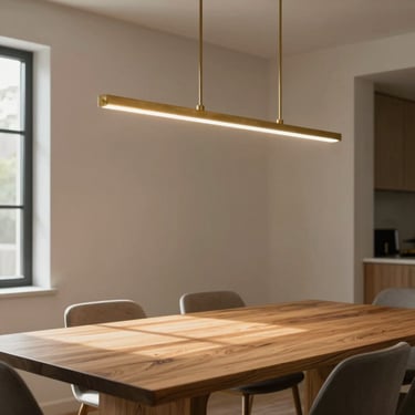 High-end residential dining room, a linear brass chandelier casting warm light on a raw oak table, soft window shadows.