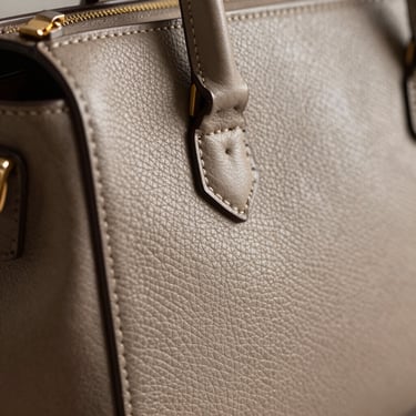 Close-up of fine stitching on a structured leather handbag, soft side-lighting highlighting texture.