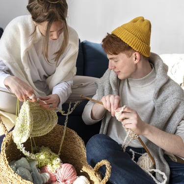 dos personas tejiendo con agujas con una canasta de estambres