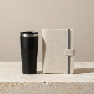 Elegant corporate gift set with a matte black tumbler and linen notebook arranged neatly on a stone surface, neutral background, 35mm