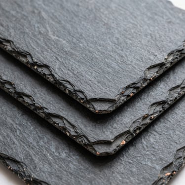 Macro shot of hand-cut natural slate tiles stacked, dark grey texture, overcast natural light
