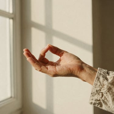 Soft hands of a mature woman in a calm mudra gesture, wearing a simple linen sleeve, warm golden-hour window shadows, 35mm film texture.