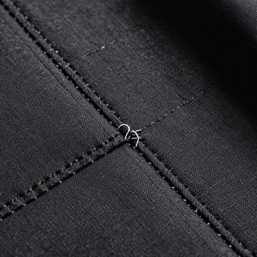 Close-up of heavy technical textile weave and reinforced stitching, dark charcoal fabric under harsh directional light.