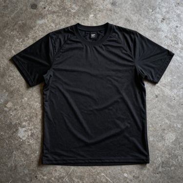 Technical black training shirt laid flat on a concrete surface, displaying reinforced shoulder stitching, high-contrast lighting