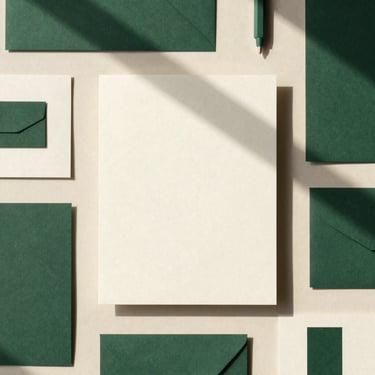 Overhead flat-lay of a complete brand stationery suite on heavy cream paper, deep green ink, natural shadows, tactile editorial style.