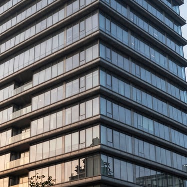 Modern commercial mid-rise facade, sharp steel cantilevers, expansive glass reflecting soft evening light, unpeopled.