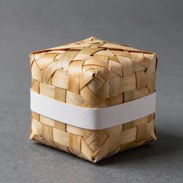 A hand-woven pandan box with a modern minimalist paper sleeve, clean editorial studio lighting.