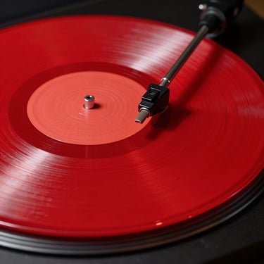 Extreme close-up of a hyper-vivid neon red vinyl record spinning under hard direct studio flash with sharp drop shadows.