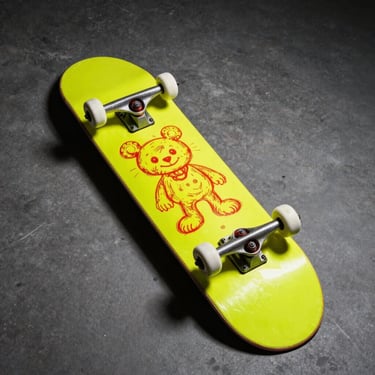 Wide-angle studio shot of a neon yellow skateboard deck with hand-drawn red marker illustrations, direct flash.