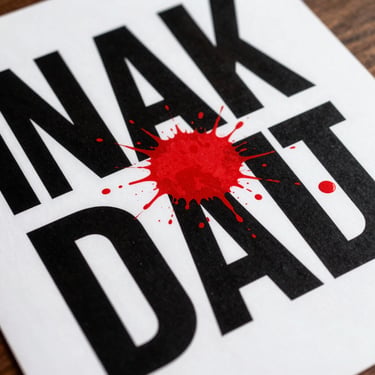 Dutch angle shot of a bold graphic poster featuring heavy black typography and explosive red ink splatters on white paper.