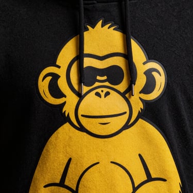 Extreme close-up of a streetwear hoodie with a giant bright yellow monkey graphic, hard studio lighting, high contrast.